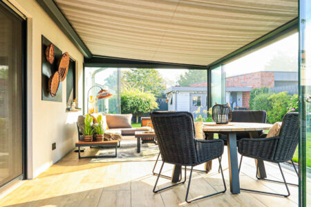 Perfektes Outdoorliving dank Terrassenüberdachnung mit Panorama-Schiebewänden aus Glas und Unterglas-Markise mit Gewebetuch im Streifenlook