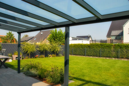 Schlichtes Terrassendach in Bedburg-Hau Hasselt mit Glaseindeckung und Blick in die liebevoll gestaltete Grünanlage